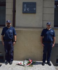 Na fotografii widać wmurowaną w ścianę tarnogórskiej komendy tablicę pamięci oraz stojących obok niej na baczność dwóch policjantów. Pod tablicą zostały złożone kwiaty.