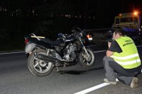 Na fotografii widać drogę, na której znajduje się rozbity motocykl. Przed motocyklem, na drodze klęczy policjant, który wykonuje zdjęcie jednośladu. Obok policjanta widać lawetę.