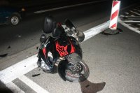 Zdjęcie przedstawia leżący na jezdni motocykl. Motocykl jest uszkodzony z uwagi na zderzenie z samochodem osobowym.