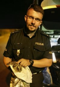 Na fotografii widać policjanta, który w rękach trzyma owiniętą w koc foliowy sowę