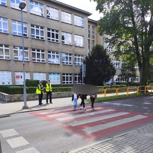 policjanci przy przejściu dla pieszych po którym idą trzy osoby. w tle szkoła